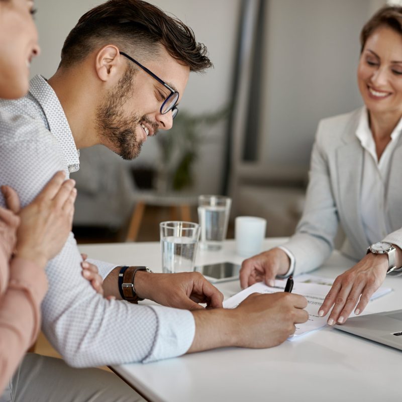 Happy man and his wife having a meeting with financial advisor and signing an agreement in the office.