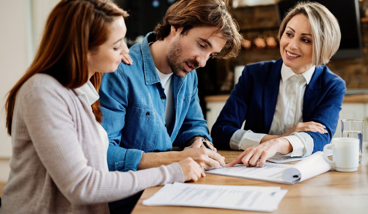 Young couple signing lease agreement while having meeting with real estate agent. Focus is on man.